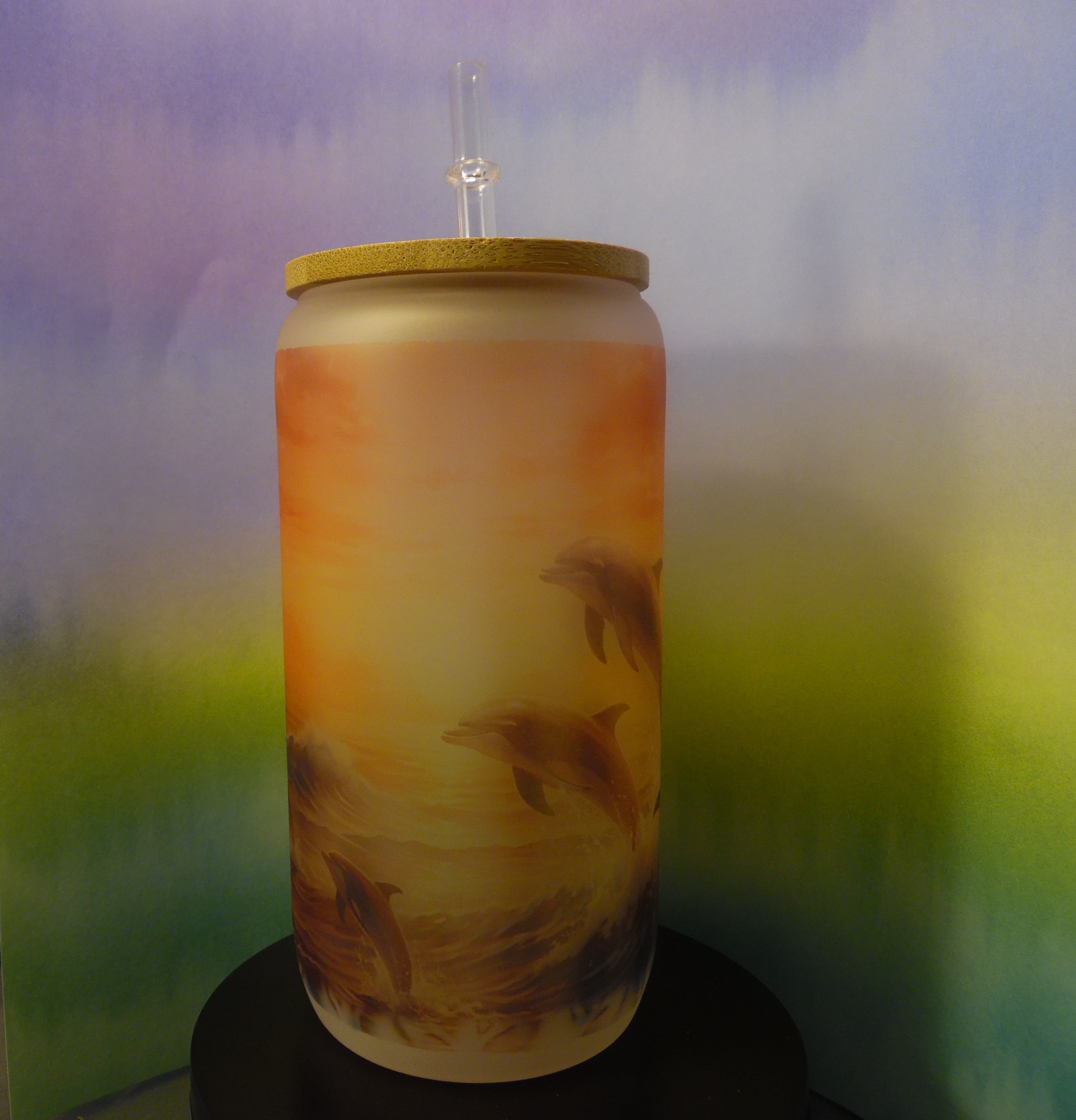 Frosted glass can cup with sunset dolphin wrap design in golden orange, peach, and teal tones, bamboo lid and plastic straw